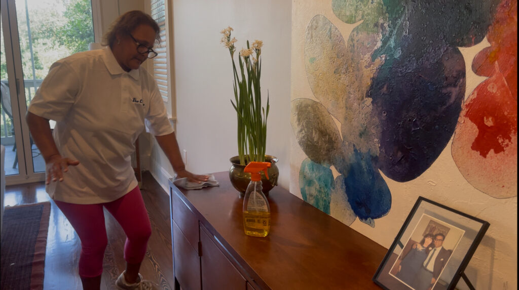Residential cleaning specialist dusting and polishing a wooden console table in a New Orleans home, part of The Cleaners’ detailed house cleaning service.